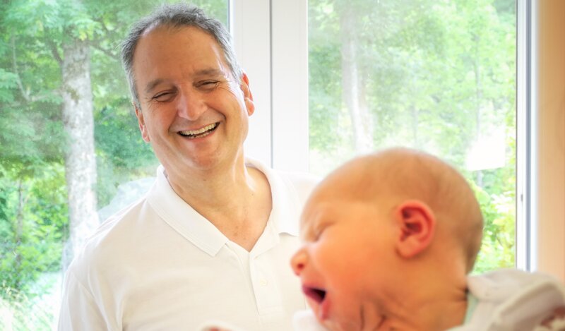 Dr. Winfried Eschholz, Chefarzt der Geburtshilfe das Krankenhauses Füssen, im Gespräch mit einer Mutter, die ihr Baby auf dem Arm hält.